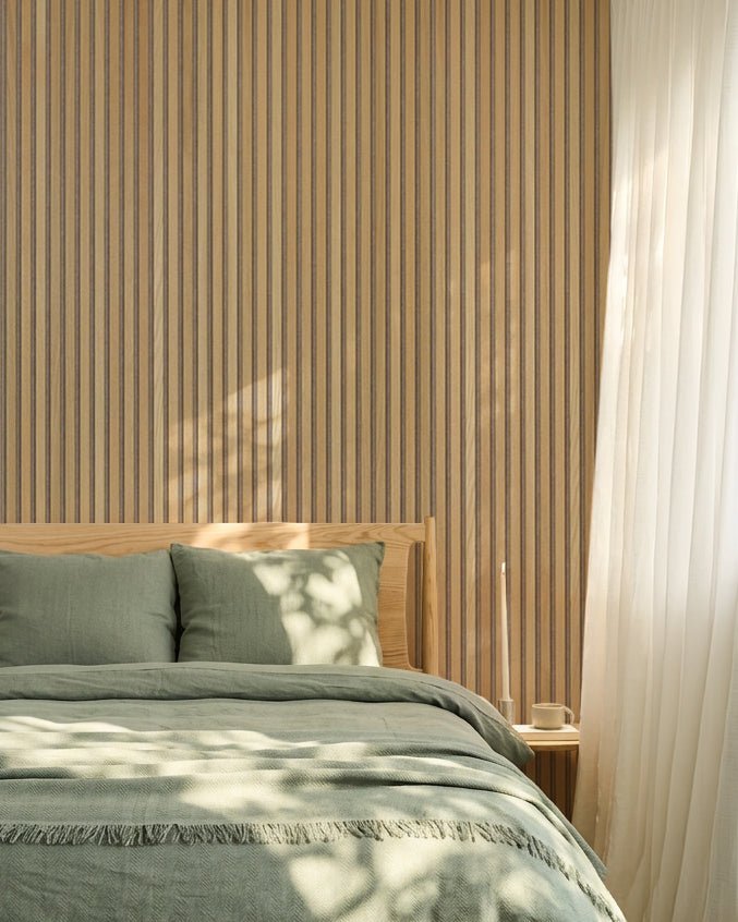 Minimalistisches nordisches Schlafzimmer mit einer WoodUpp Akupanel Eichenwand Akustikpaneel, salbeigrüner Bettwäsche, Holzbettrahmen und transparenten weißen Vorhängen.