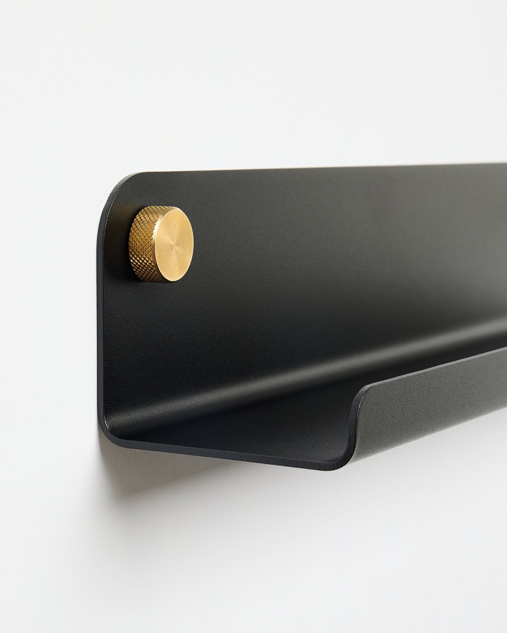 Das Norr | schmale Regal in black (115,9 cm) mit einem einzelnen goldenen Knauf links, von WoodUpp, montiert an einer schlichten weißen Wand.