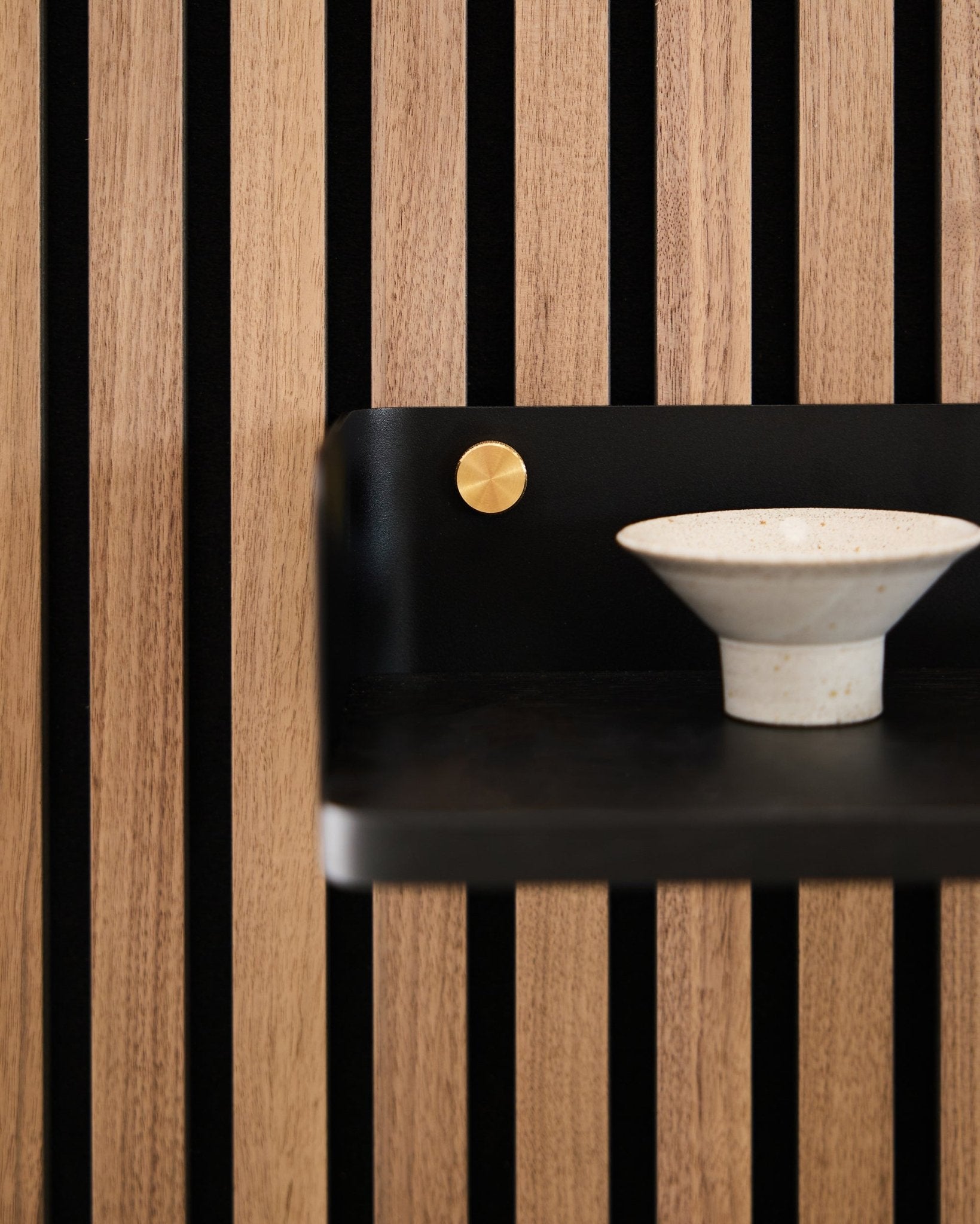 Eine Keramikschale steht auf dem Linn Bücherregal von WoodUpp, 39,9 cm in black oak, mit vertical black Lamellen und einem Akzent in brass, was nordisches minimalistisches Design widerspiegelt.