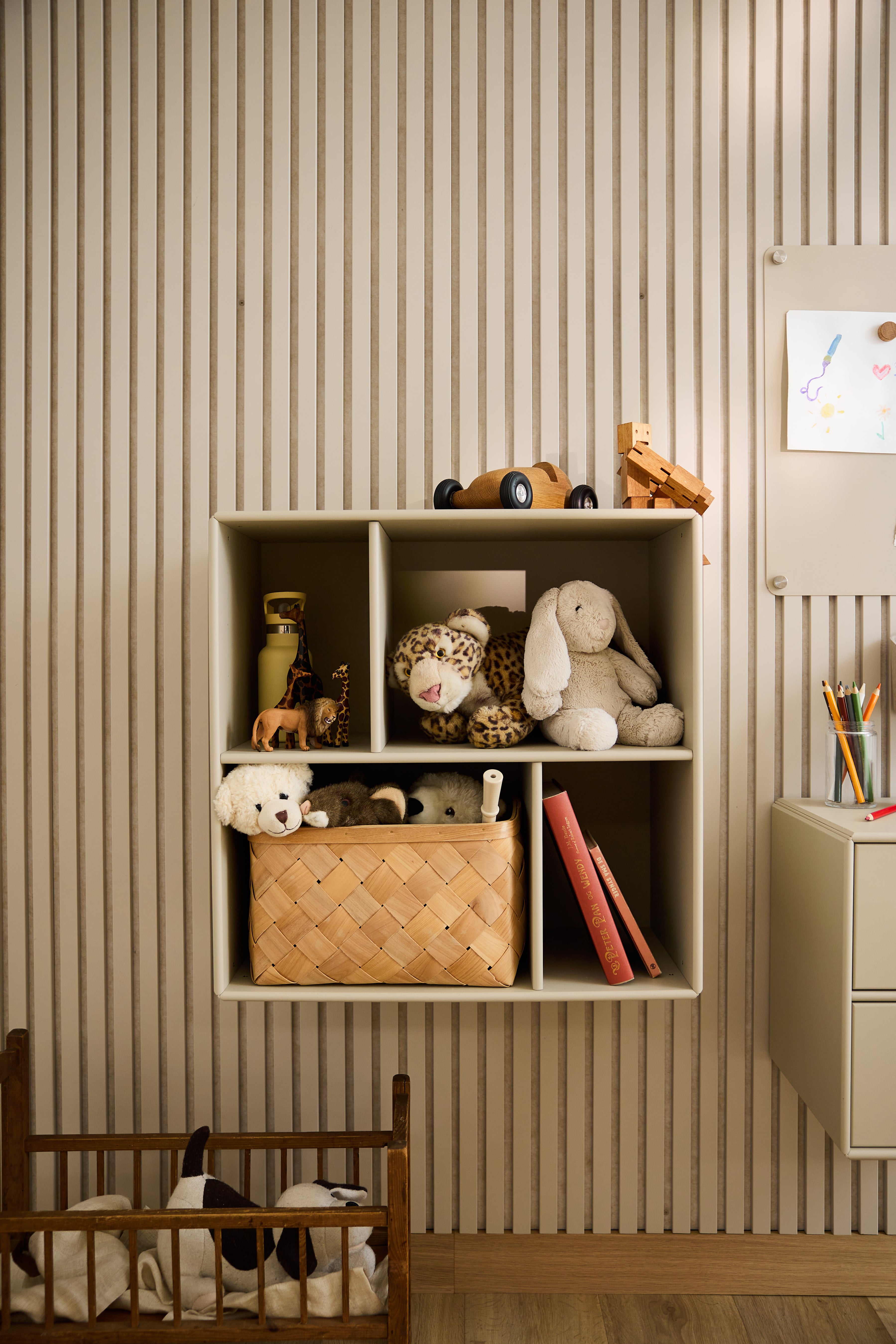 Der offene Schrank Arka von WoodUpp in Beige mit Spielzeug und Büchern vor einer gestreiften Tapete in einem Kinderzimmer verkörpert minimalistisches nordisches Design.