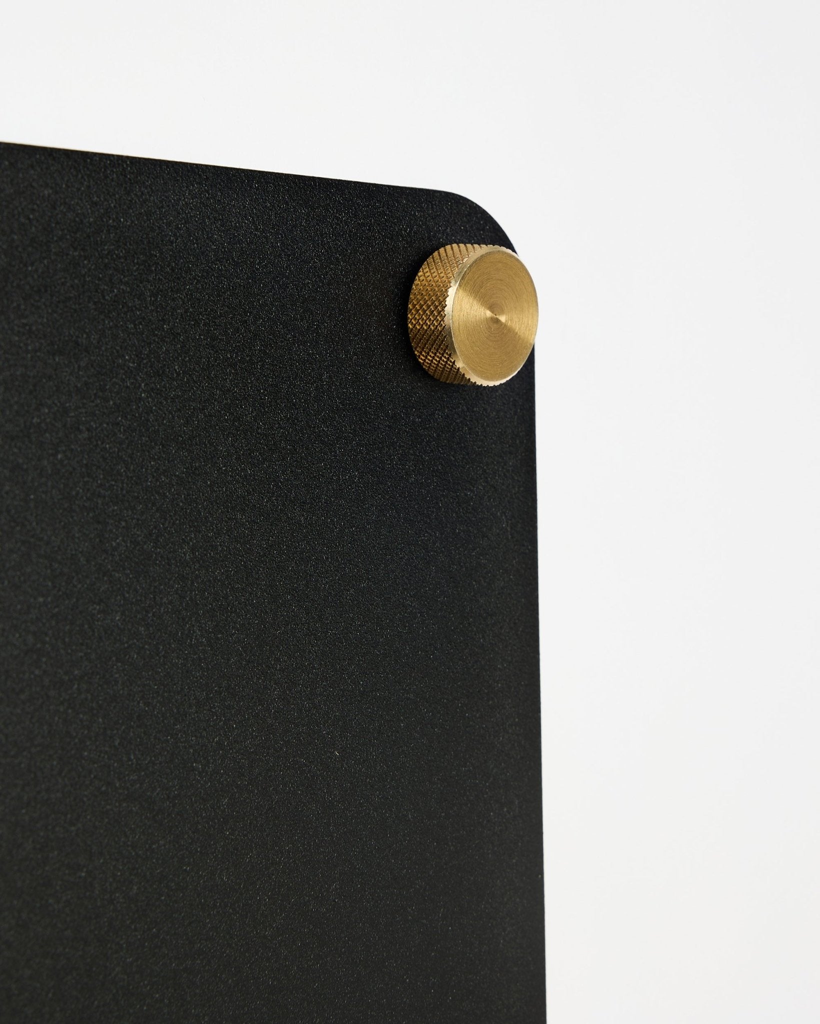 Nahaufnahme der WoodUpp Norr black Akustik-Magnettafel (small) mit abgerundeter Ecke und goldener Schraubbefestigung vor weißem Hintergrund.