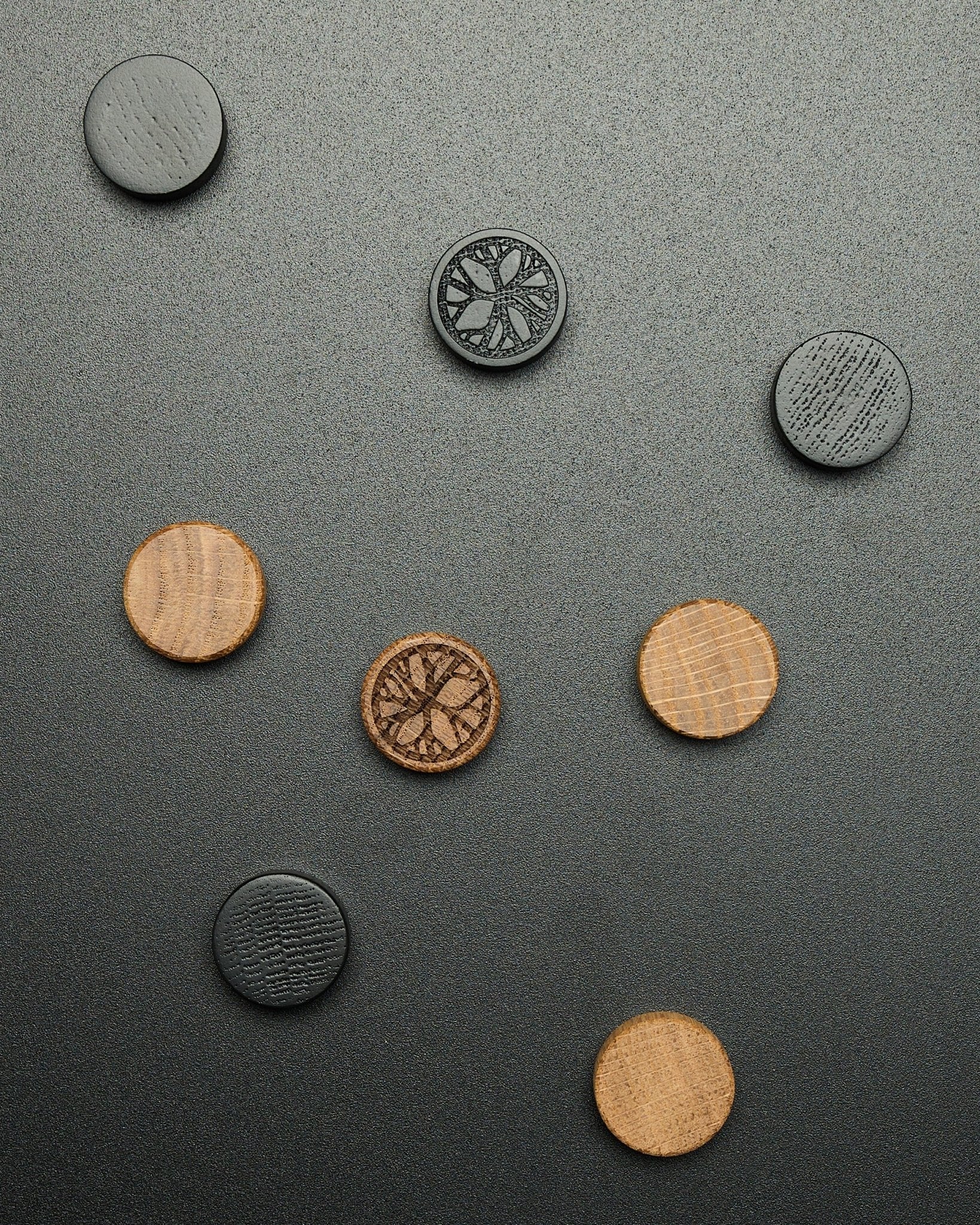Vier runde black oak Magnete aus dem WoodUpp Norr Magnet-Set, locker auf einer strukturierten dunklen Oberfläche angeordnet, gedacht als Akupanel Accessoires.