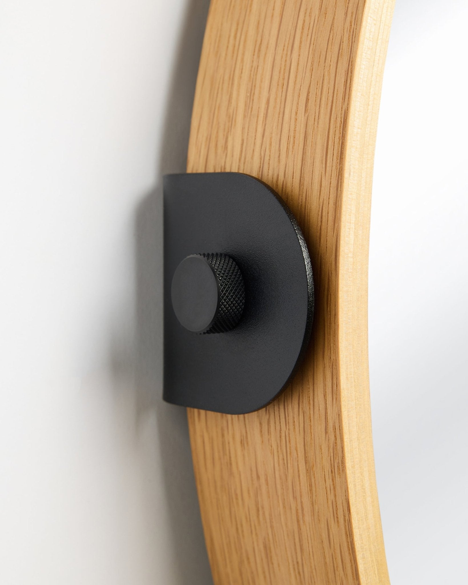 Detail des WoodUpp Linn Spiegels in Natural Oak, ein Akustikpaneel, das mit einer Metallhalterung in black und rundem Knauf an der Wand montiert ist.