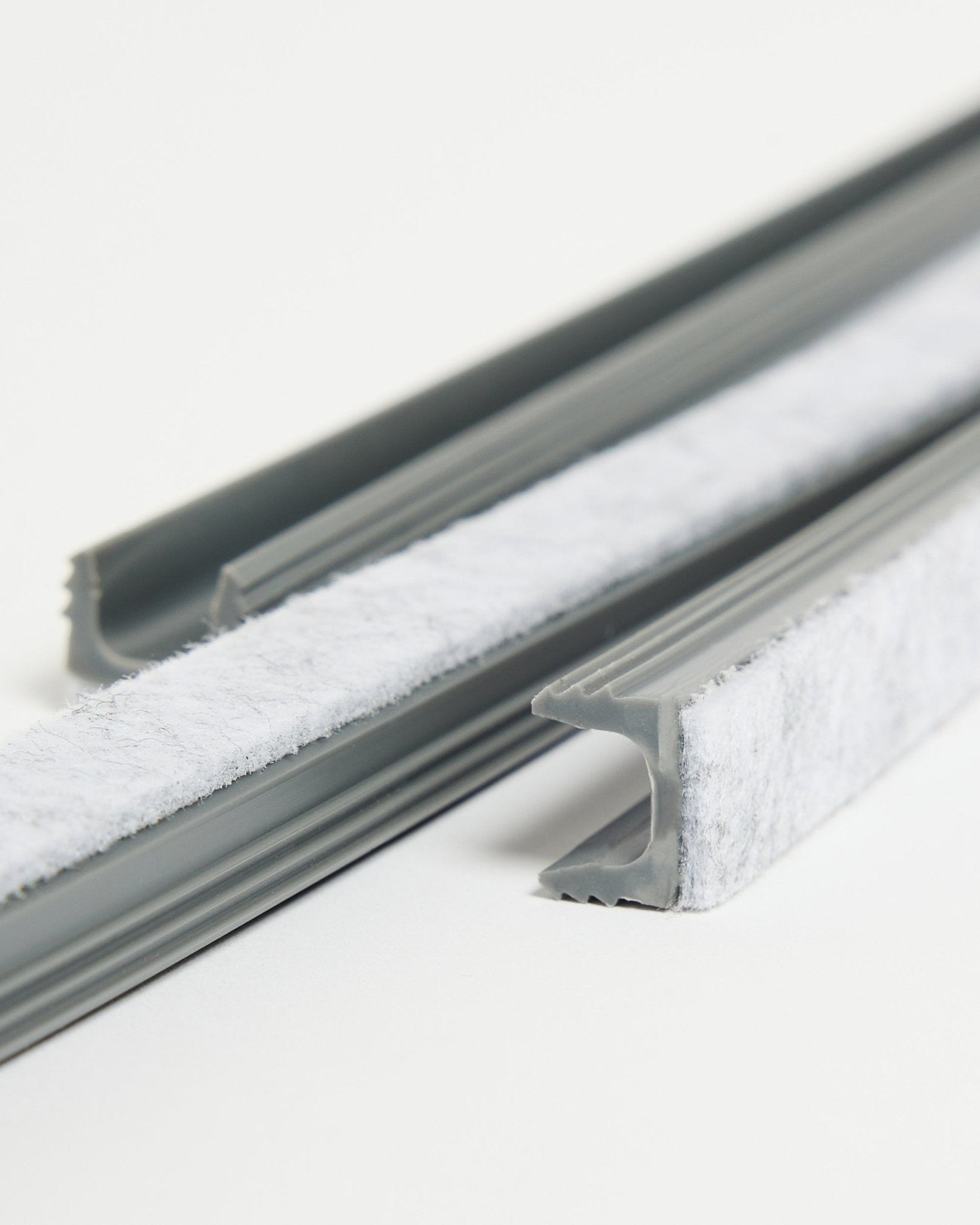 Drei graue WoodUpp Dupps Pop-on Cable Covers mit weißer Dichtung und flexiblen TPV-Kanälen liegen auf einer weißen Oberfläche.