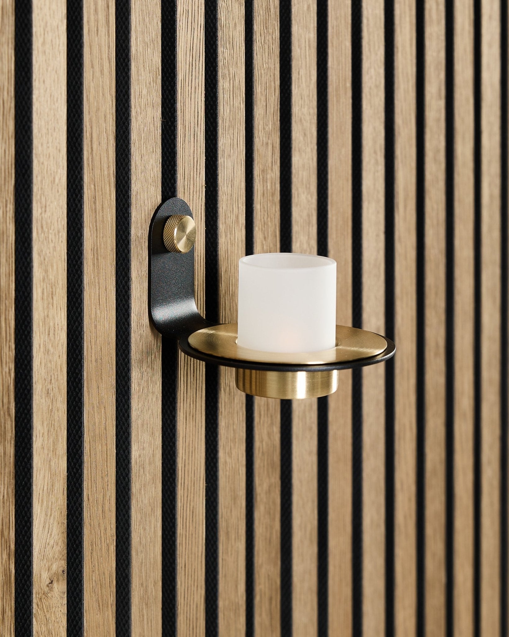 Der Norr Kerzenhalter in black und brass von WoodUpp ist auf einem nordischen Akupanel Akustik-Holzpaneel mit vertical black Lamellen montiert.