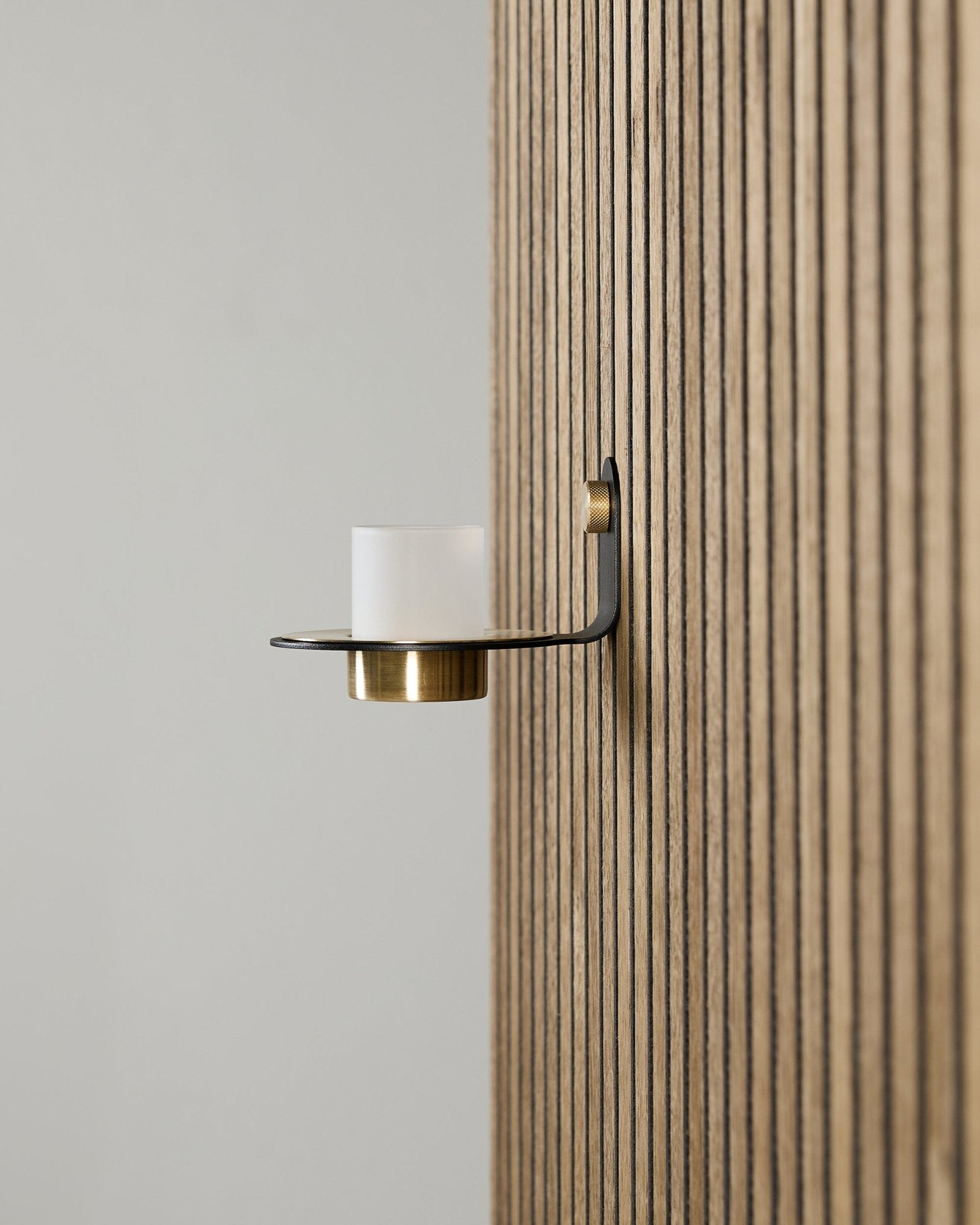 Norr Kerzenhalter in black und brass von WoodUpp, montiert auf einem vertical Akupanel Akustikpaneel, mit Milchglas und brass Details.