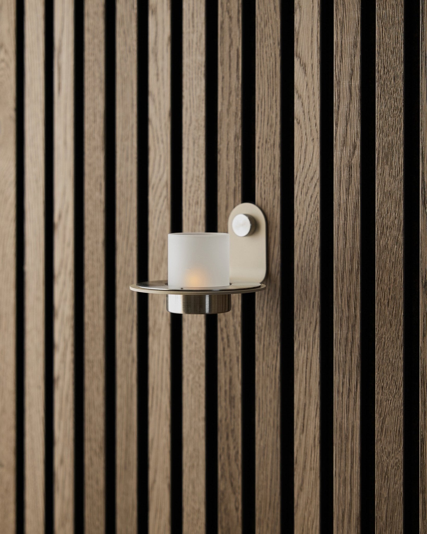 Der Norr Kerzenhalter aus beige Edelstahl von WoodUpp, präsentiert an einer beige Akupanel Akustikpaneel Wand.