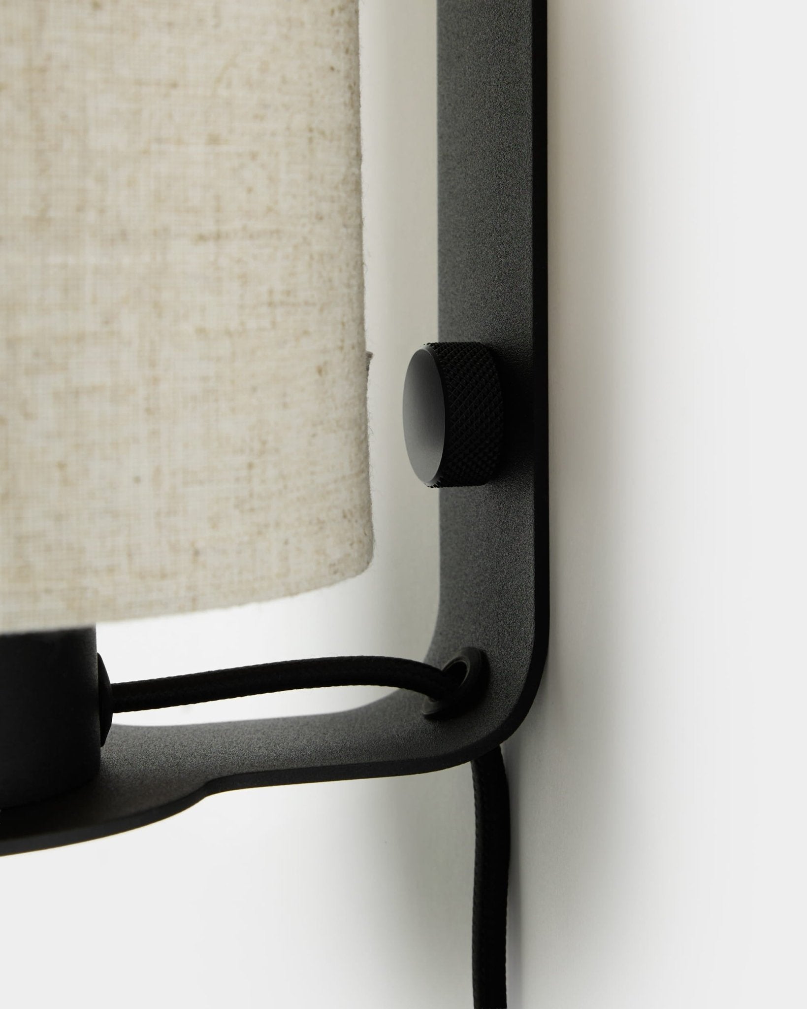 Nahaufnahme der WoodUpp Feya Wandleuchte in black und beige mit strukturiertem Drehknopf, Leinenschirm aus Baumwollmischung und sichtbarem Kabel, montiert an einer weißen Wand.