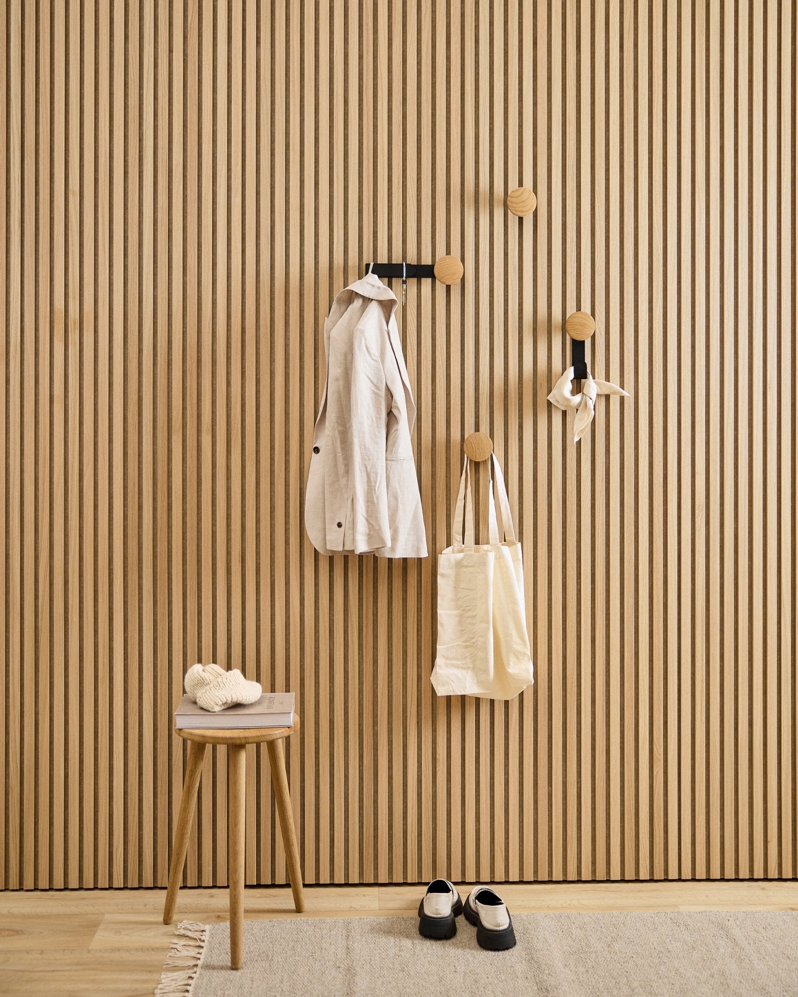 Minimalistischer Eingangsbereich mit dem WoodUpp Linn Vertical Hanger in natural oak, dazu ein beige Mantel, eine Tragetasche, ein Schal, ein Hocker mit Hausschuhen und black-weiße Schuhe.