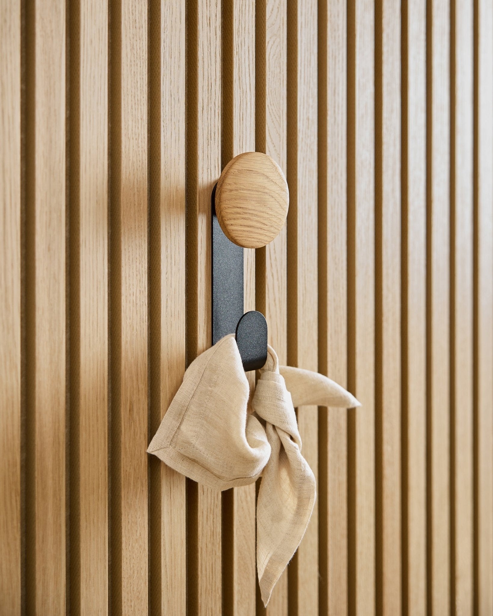 Ein beige Tuch hängt am Linn Vertical Hanger in Natural Oak von WoodUpp, montiert an einem vertical Akupanel Akustik-Lamellenpaneel.