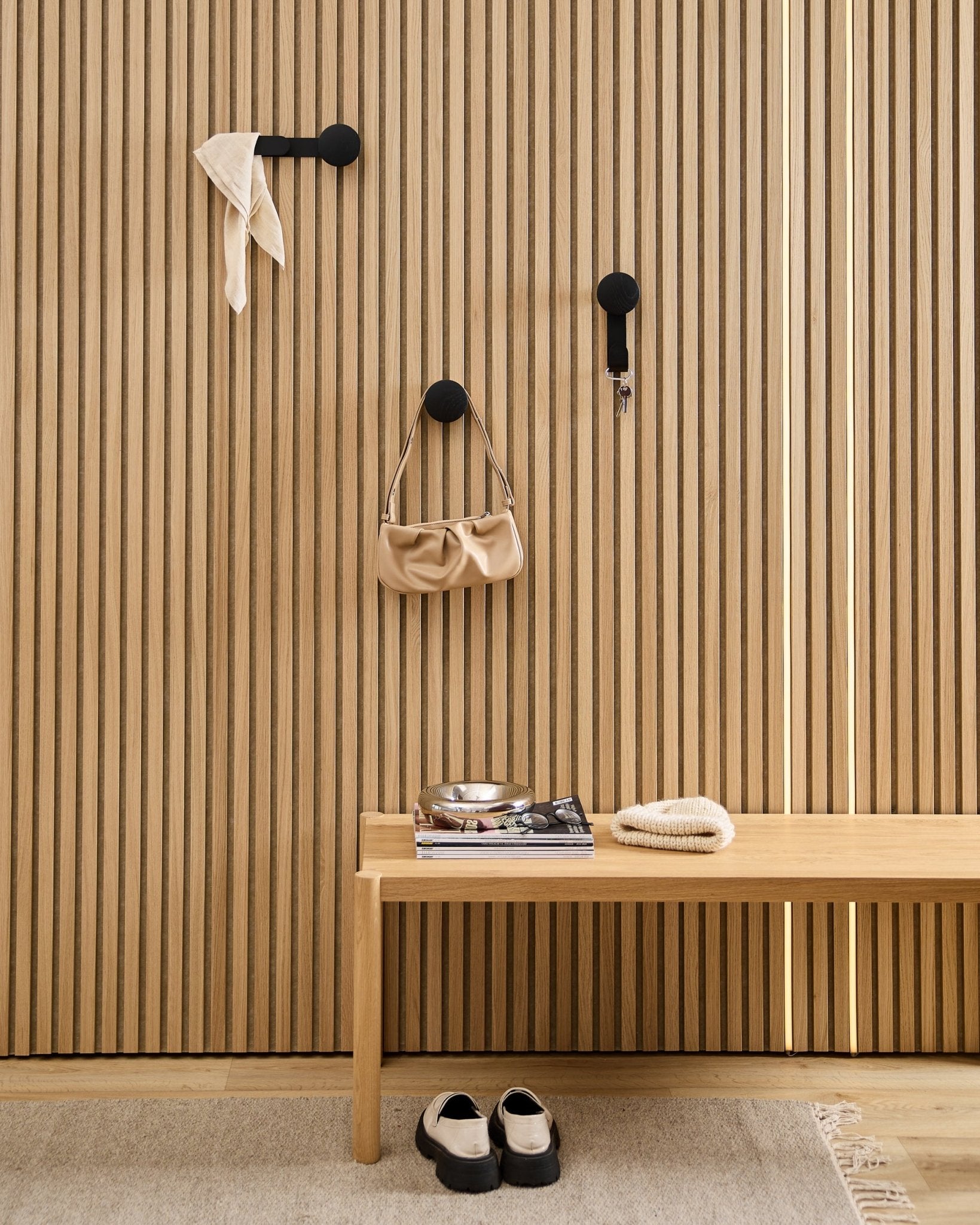 Minimalistischer Eingangsbereich mit einem WoodUpp Linn Horizontal Hanger in Black Oak mit black Haken, Holzbank, Schuhen, Büchern und einer Schale. Nordischer Stil.