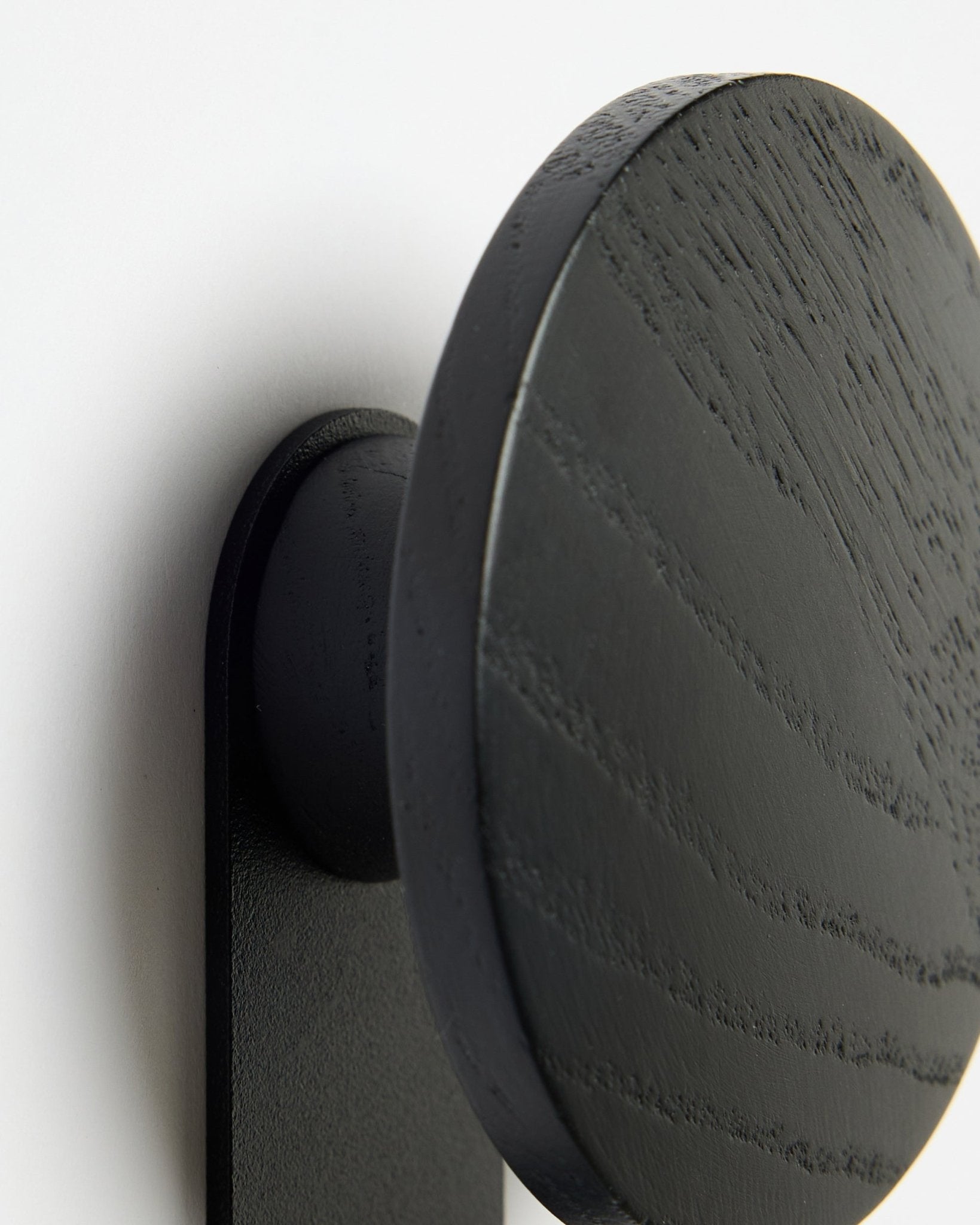 Nahaufnahme des WoodUpp Linn | Vertical Hakens in Black Oak, die die detaillierte Holzmaserung vor einem weißen Akupanel Akustikpaneel Hintergrund hervorhebt.