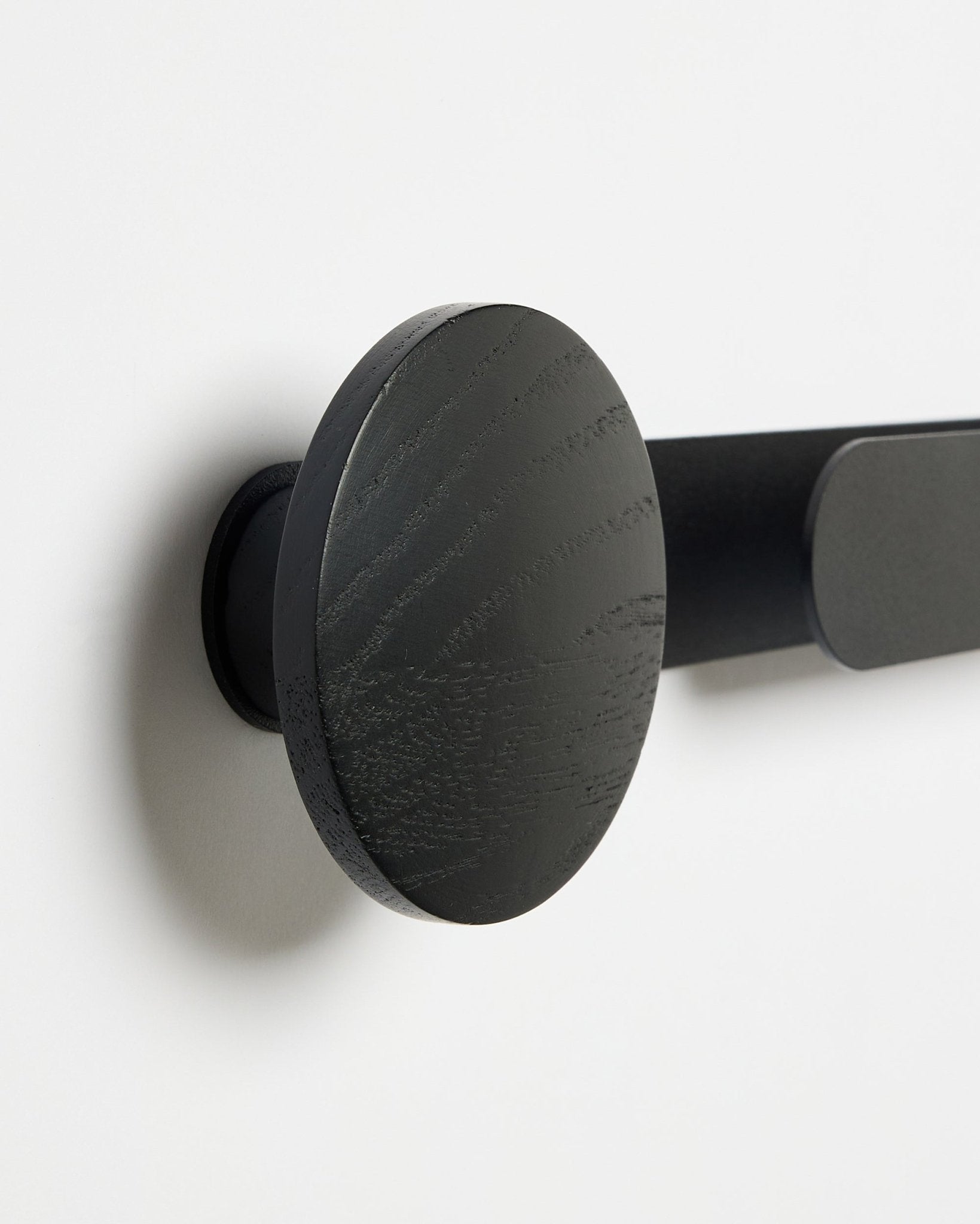 Nahaufnahme des WoodUpp Linn | Horizontal Hanger in Black Oak mit matter black Oberfläche, an einer weißen Wand montiert; Zubehör für Akustik-Holzpaneele.