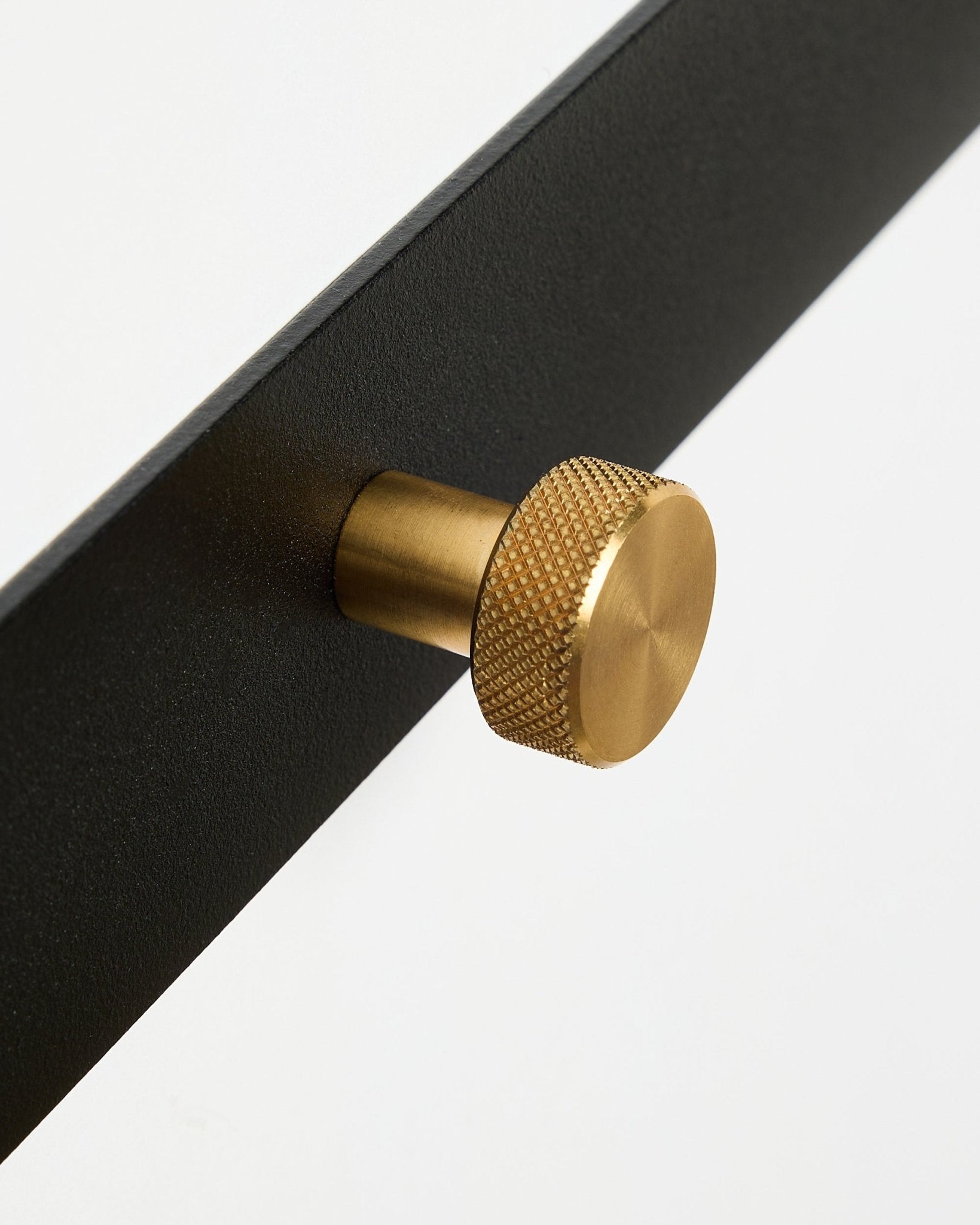 Nahaufnahme der Norr Garderobenleiste X5 von WoodUpp mit black pulverbeschichtetem steel und runden, strukturierten brass Knöpfen, vor einem weißen Hintergrund.