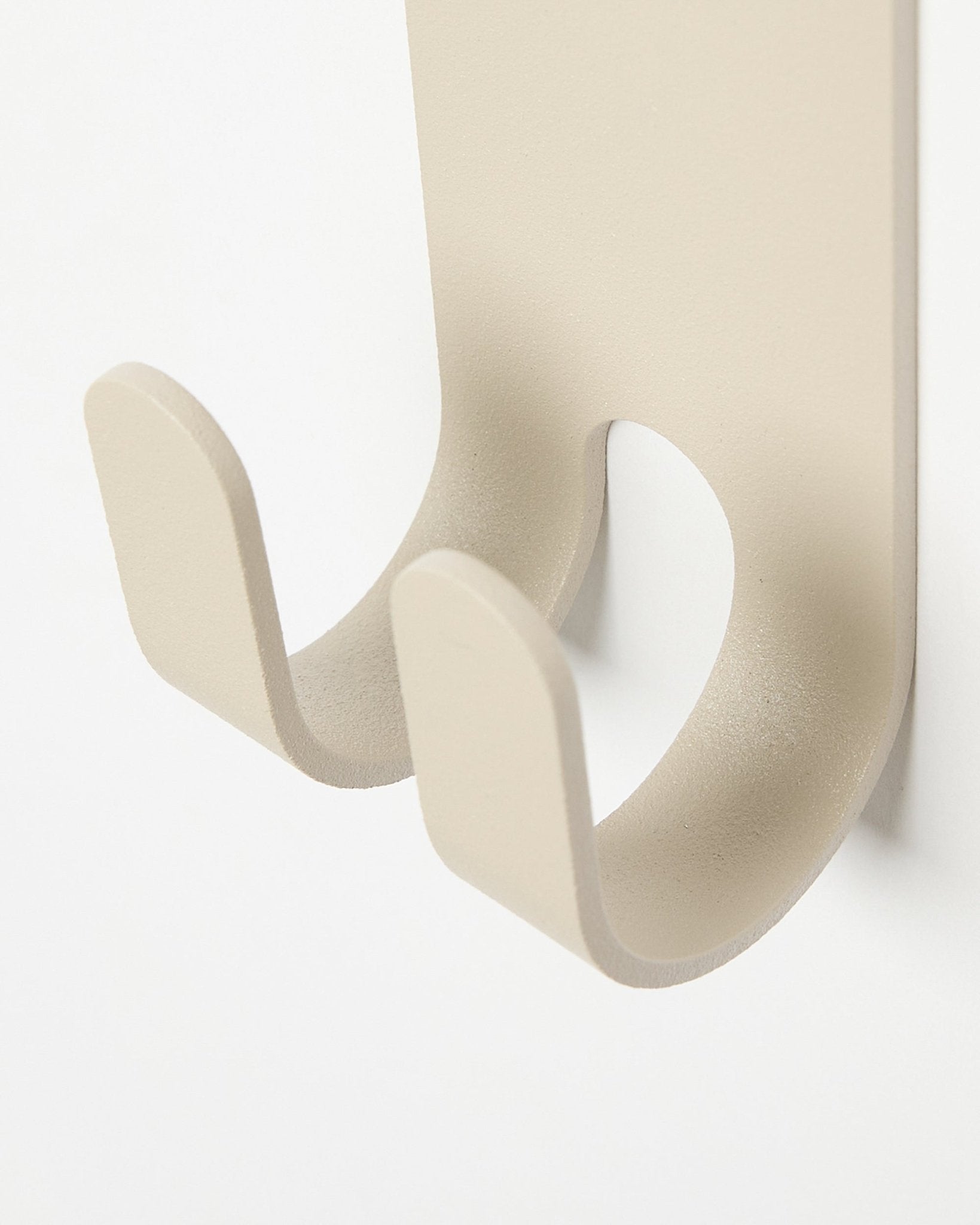 Nahaufnahme der Norr Double Hanger in beige von WoodUpp, ein minimalistischer Metallhaken, installiert auf einem hellen colored Akustikpaneel.