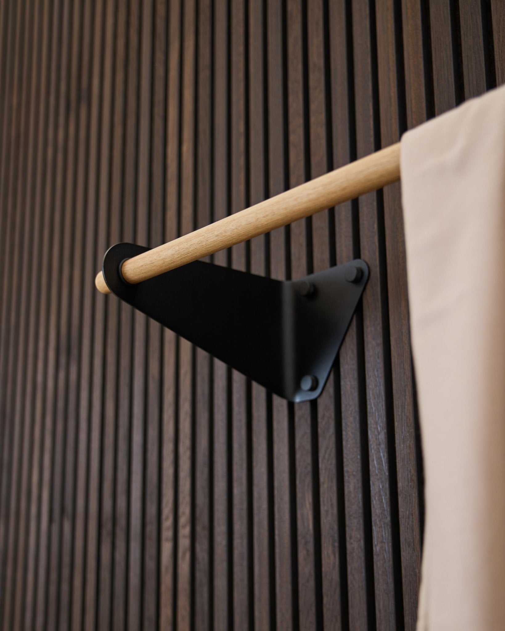 Linn Kleiderstange von WoodUpp in black (115,9 cm), montiert auf einem dunklen gerillten Akupanel Akustikpaneel, mit Stoffakzent in beige und Halterung in black.