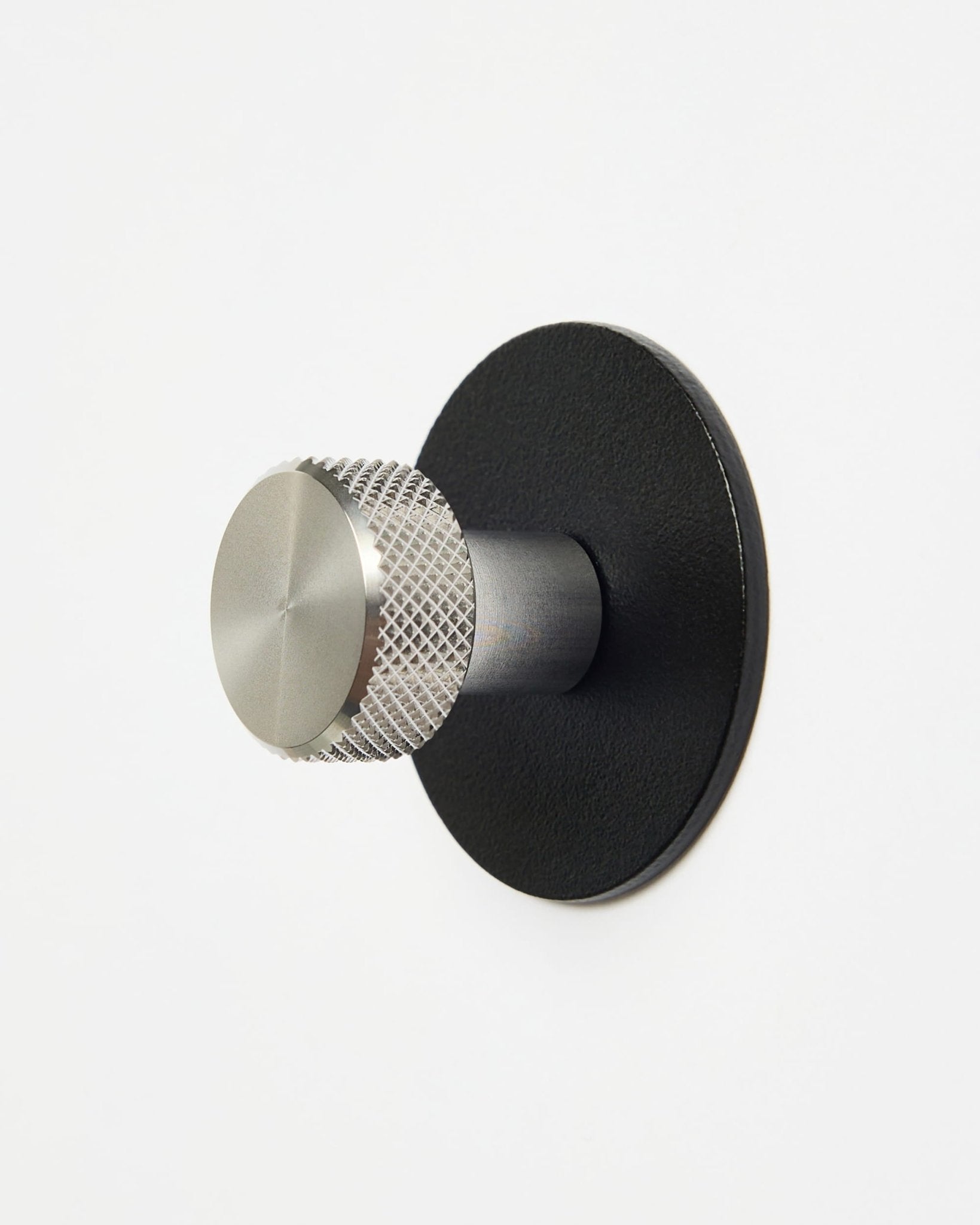 WoodUpp Norr | Coat Hook X1 in black und Edelstahl steel, installiert an einer schlichten weißen Wand, entworfen als Zubehör der CREATE Kollektion für Akupanel Systeme.