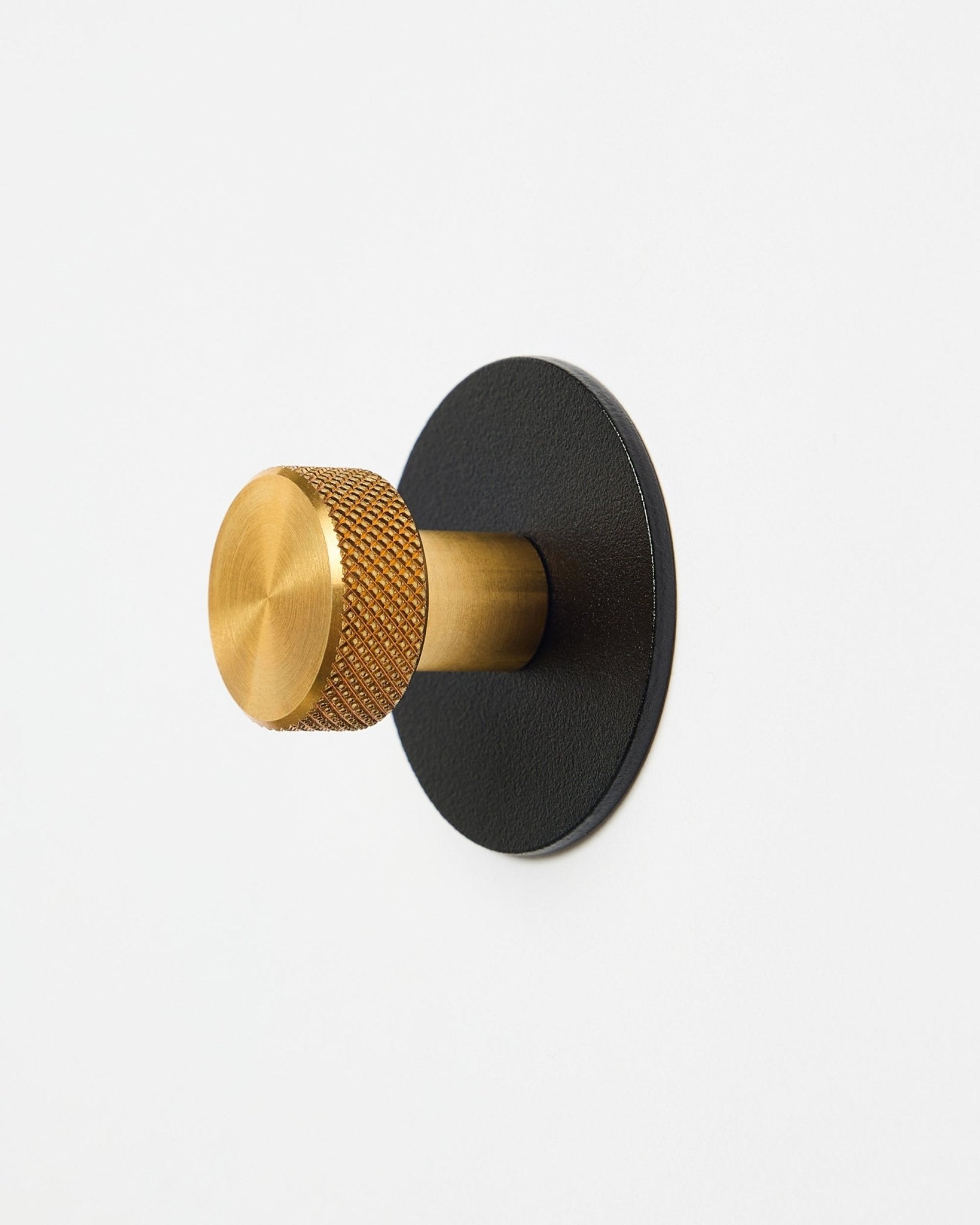 Norr Coat Hook X1 von WoodUpp mit einem strukturierten brass Knauf und einer black pulverbeschichteten steel-Basis, Accessoire für Akupanel, dargestellt vor weißem Hintergrund.