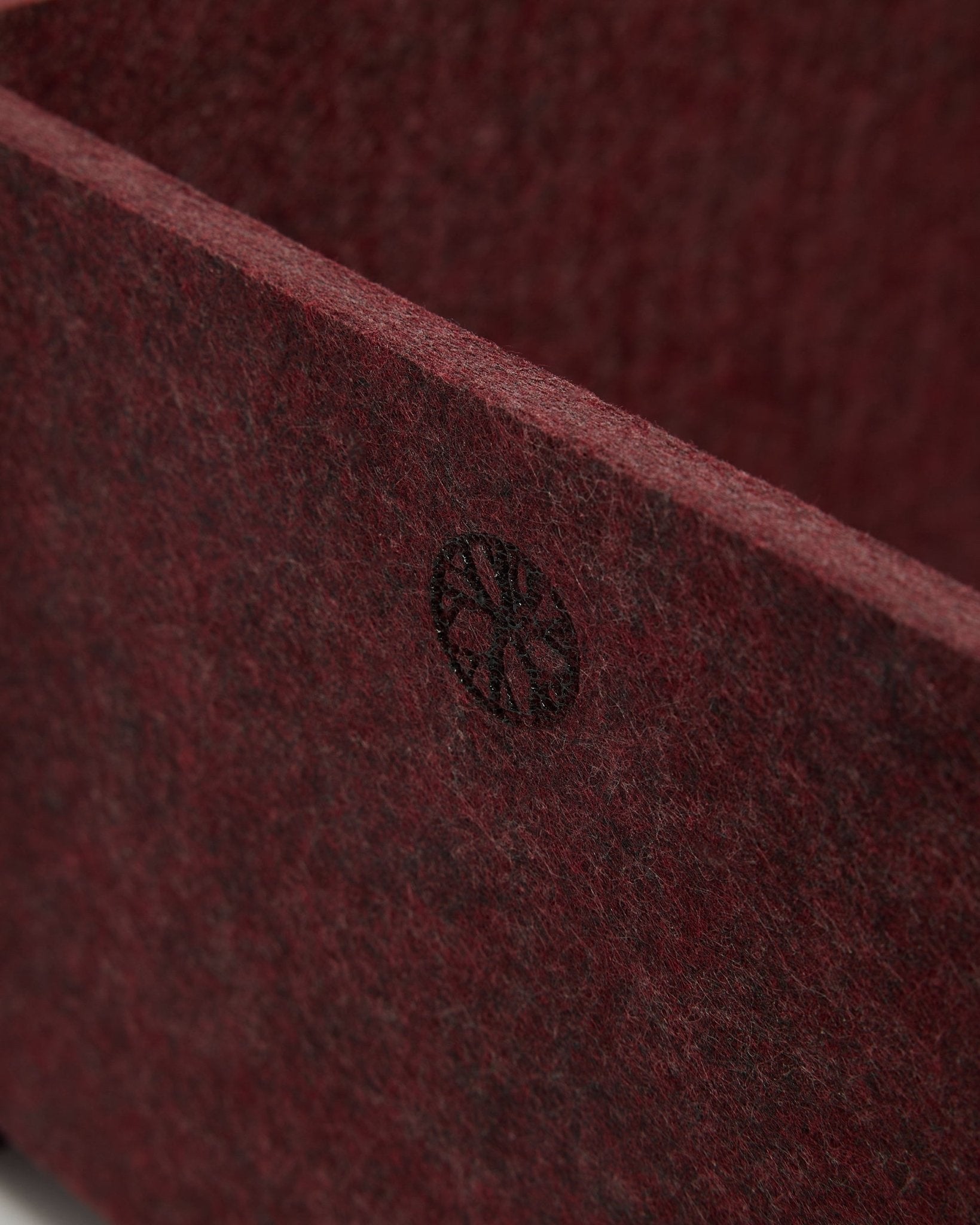 Nahaufnahme von WoodUpp Vigg | Felt Box / BM2 in ox red, die strukturierten PET-Filz und ein rundes black-Emblem in der Ecke zeigt. Nordisches Design-Akustikaccessoire.