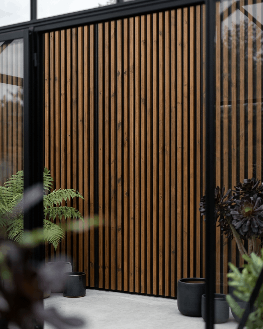 WoodUpp Aluwood Outdoor-Fassadenpaneel in geöltem brown, kombiniert mit black Pflanzgefäßen und grünen Pflanzen, für eine minimalistische nordische Terrassenatmosphäre.