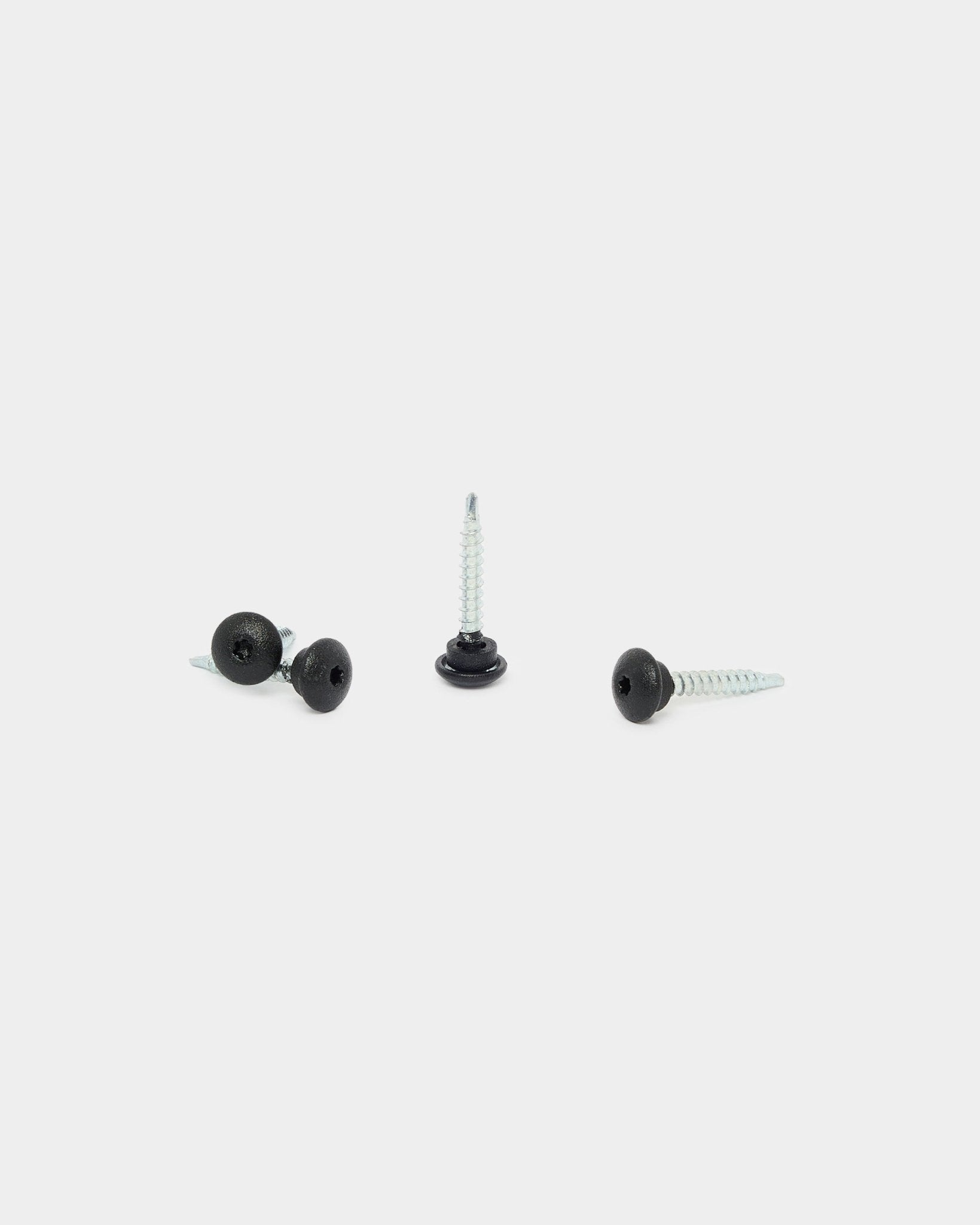 Drei black WoodUpp 4,8x35 Schrauben mit Ø9,5 Unterlegscheiben auf weißem Hintergrund, vorgesehen als Befestiger für Aluwood Outdoor-Fassadenpaneele.