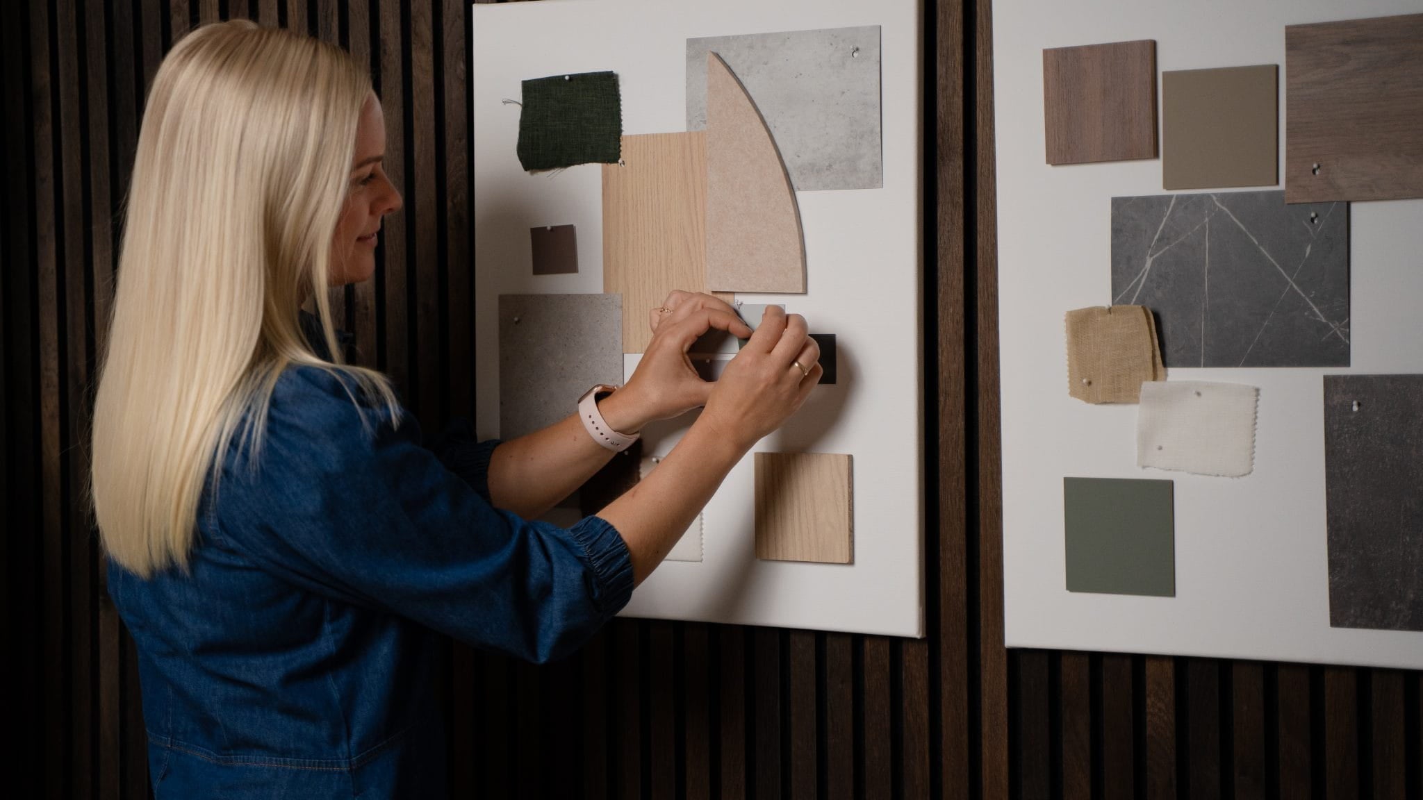 Eine Frau ordnet Stoff- und Farbmuster auf einem Moodboard an, daneben befindet sich ein weiteres Inspirationsboard, neben dem Akustikholzplatten aus der Akupanel-Kollektion von WoodUpp liegen.