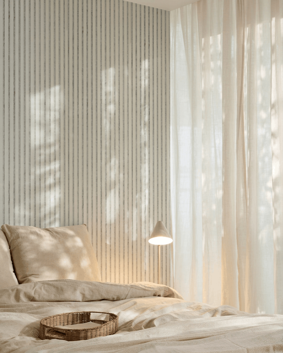 Minimalistisches Schlafzimmer mit beige Bettwäsche, einem Korbtablett, gestreifter Tapete und einem WoodUpp Akupanel Akustik-Holzpaneel in Snow Grey Filz zur Schallabsorption.