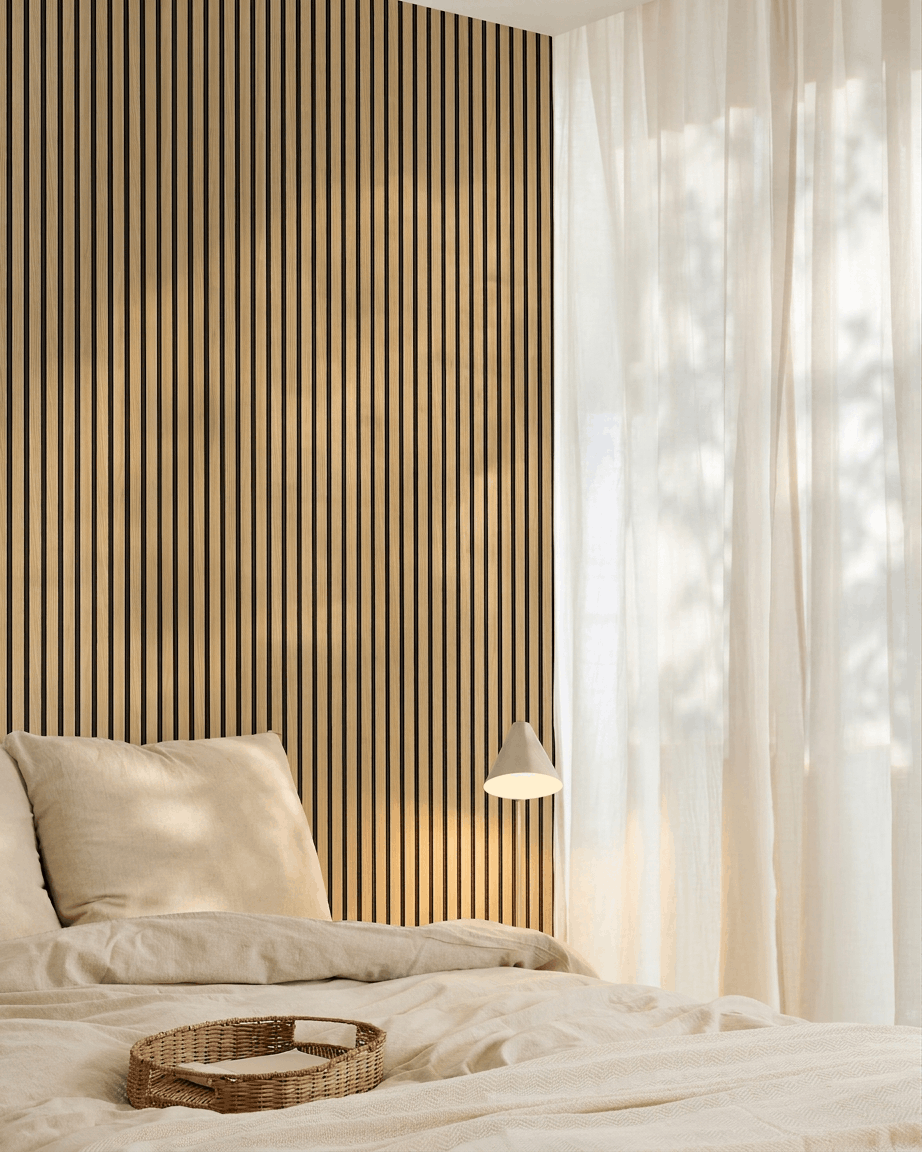 Minimalistisches Schlafzimmer mit beige Bettwäsche, einer WoodUpp Akupanel Southern Oak Akustikpaneel Akzentwand, einem geflochtenen Tablett auf dem Bett und transparenten Vorhängen, die natürliches Licht hereinlassen.