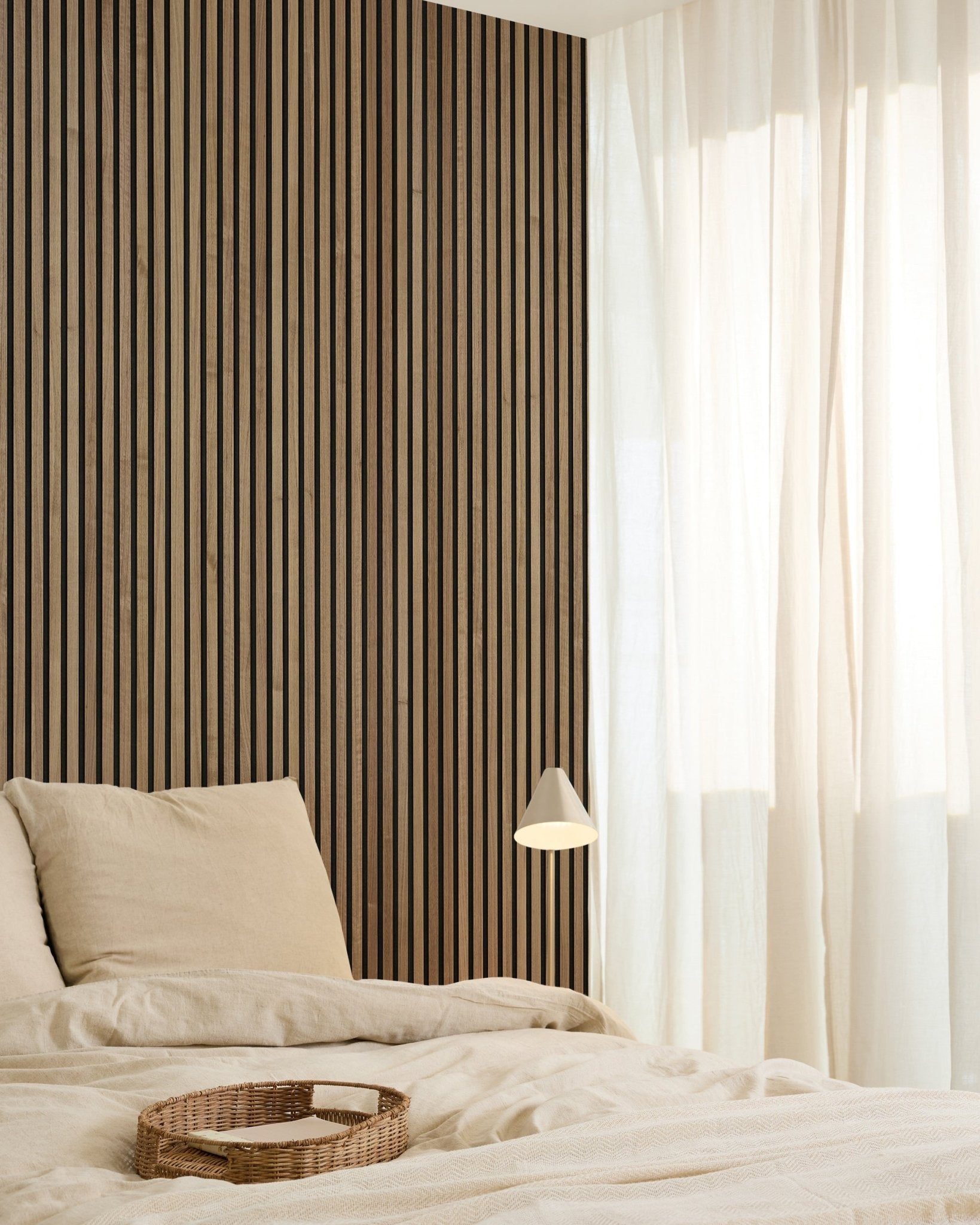 Minimalistisches Schlafzimmer mit einem WoodUpp Original Akupanel Walnut Akustikpaneel (240x60cm) an der Wand, beige Bettwäsche, transparenten Vorhängen, einem geflochtenen Tablett und einer small Wandleuchte.
