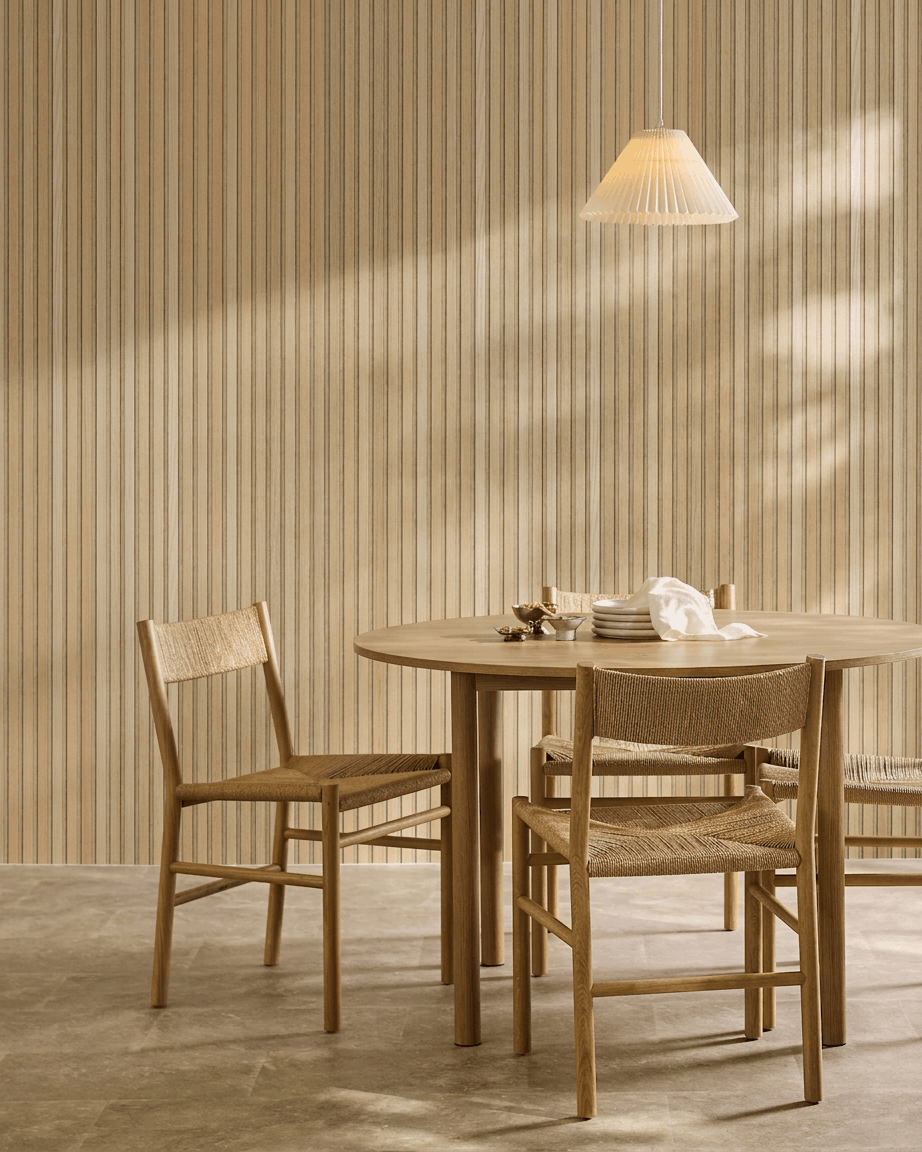 Minimalistischer Essbereich mit rundem Tisch, geflochtenen Stühlen und Pendelleuchte neben einem WoodUpp Akupanel Akustikholzpaneel in Classic Oak mit beige Filz.