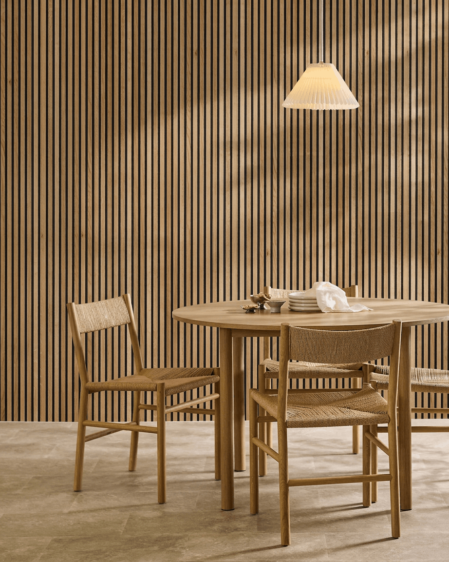 Minimalistischer Essbereich mit einem runden Tisch, geflochtenen Stühlen und einem WoodUpp Akupanel Akustik-Lamellenwandpaneel in Rustic Natural Oak als nordischem Wandakzent.