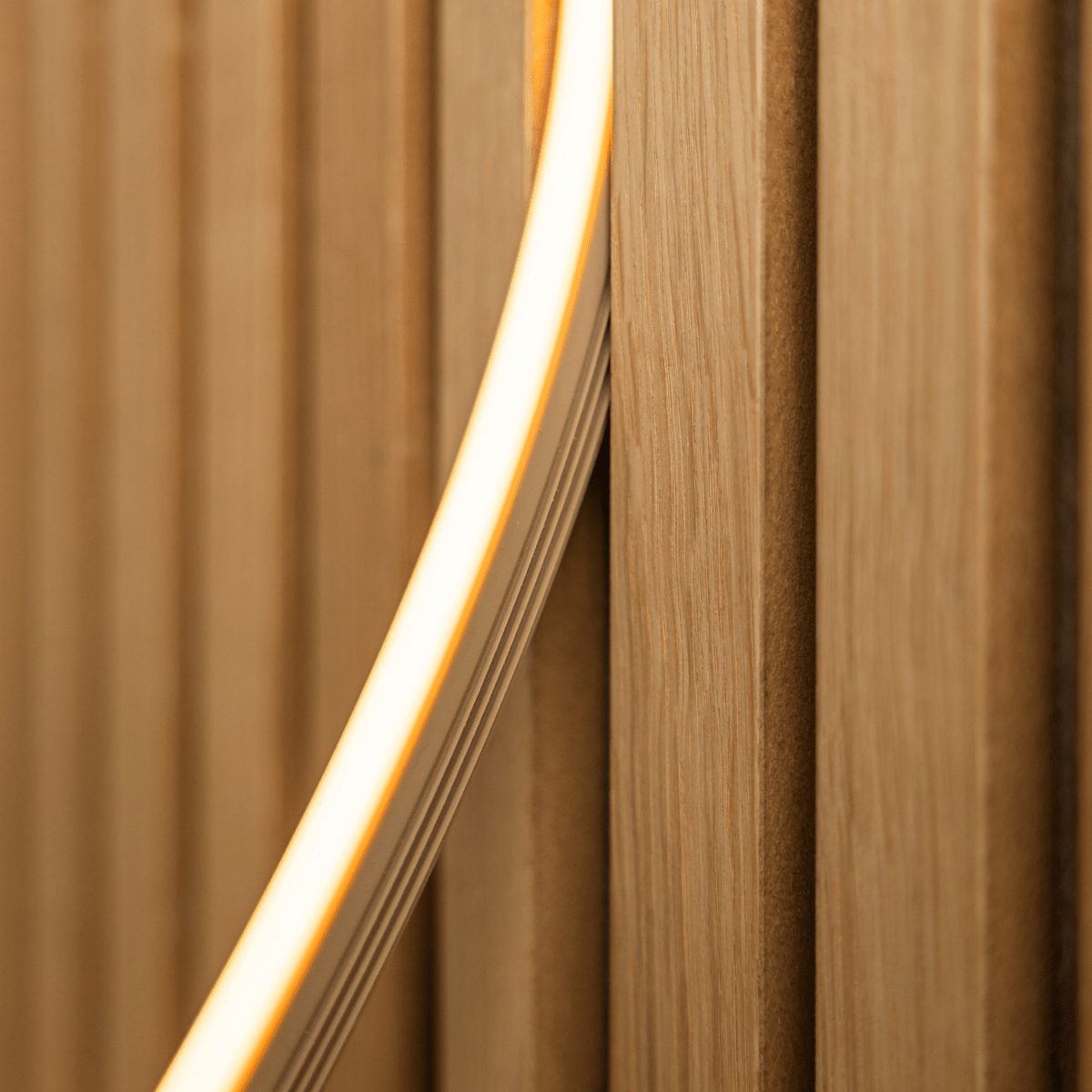 Nahaufnahme der WoodUpp Lumi LED-Lichtleiste in beige (240 cm), die warmgelbes Licht auf Akupanel vertical Akustik-Holzlamellen wirft; kompatibel mit Philips Hue.