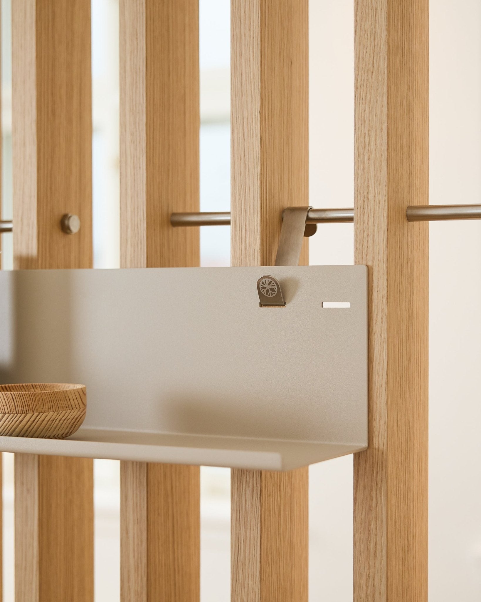 Beige WoodUpp BM1 Metallregal (63 x 13,4 cm), montiert an einem vertical Akustik-Lamellenpaneel, mit einer Holzschale auf der linken Seite der Ablage.