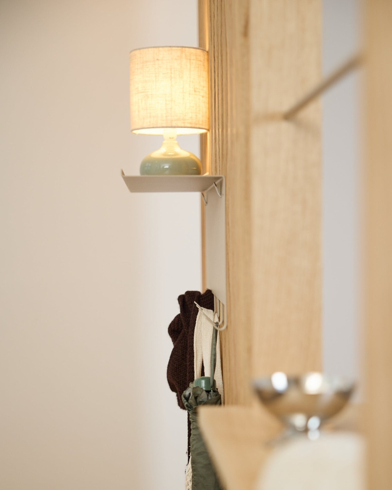 Eine beige WoodUpp Nell Garderobenleiste BM1 (63,5 x 24 cm) steht unter einer small Tischlampe neben einer hellen nordischen Holzwand Akustikpaneel.