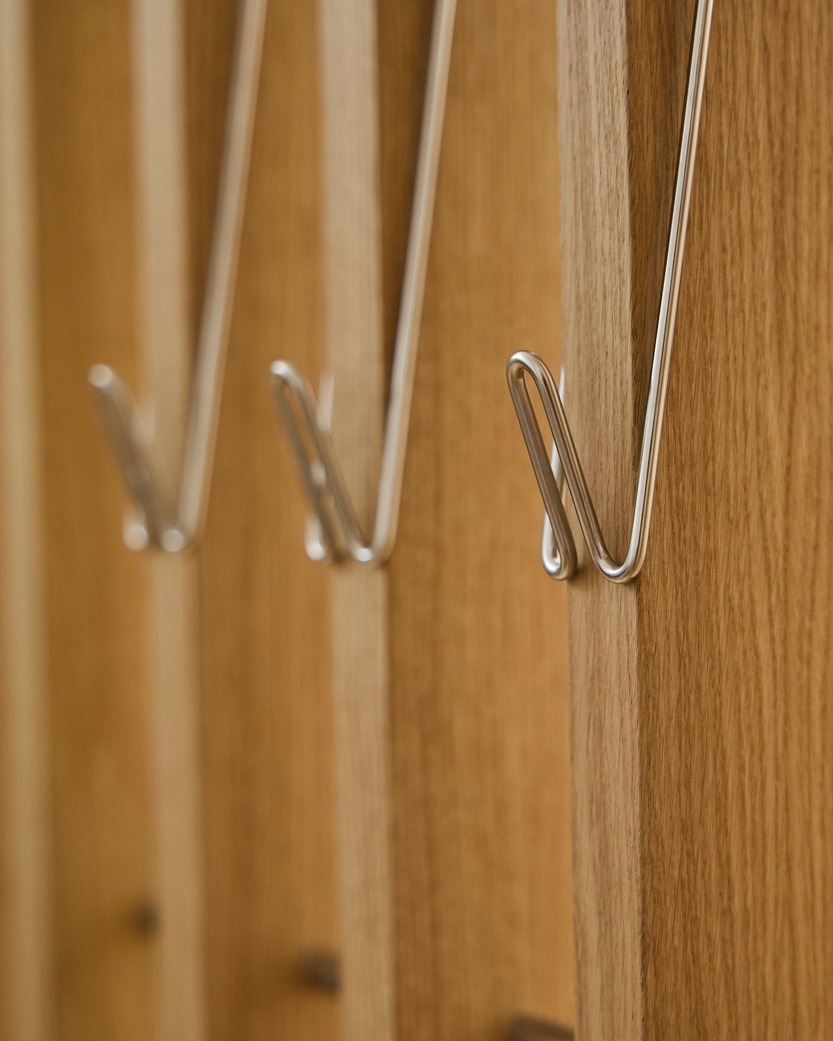 Nahaufnahme von drei Alva | Wire Hook / BM1, Edelstahl Steel, lang, von WoodUpp, in einer Reihe auf Akupanel Akustik-Holzpaneelen montiert und mit weichen Schatten.