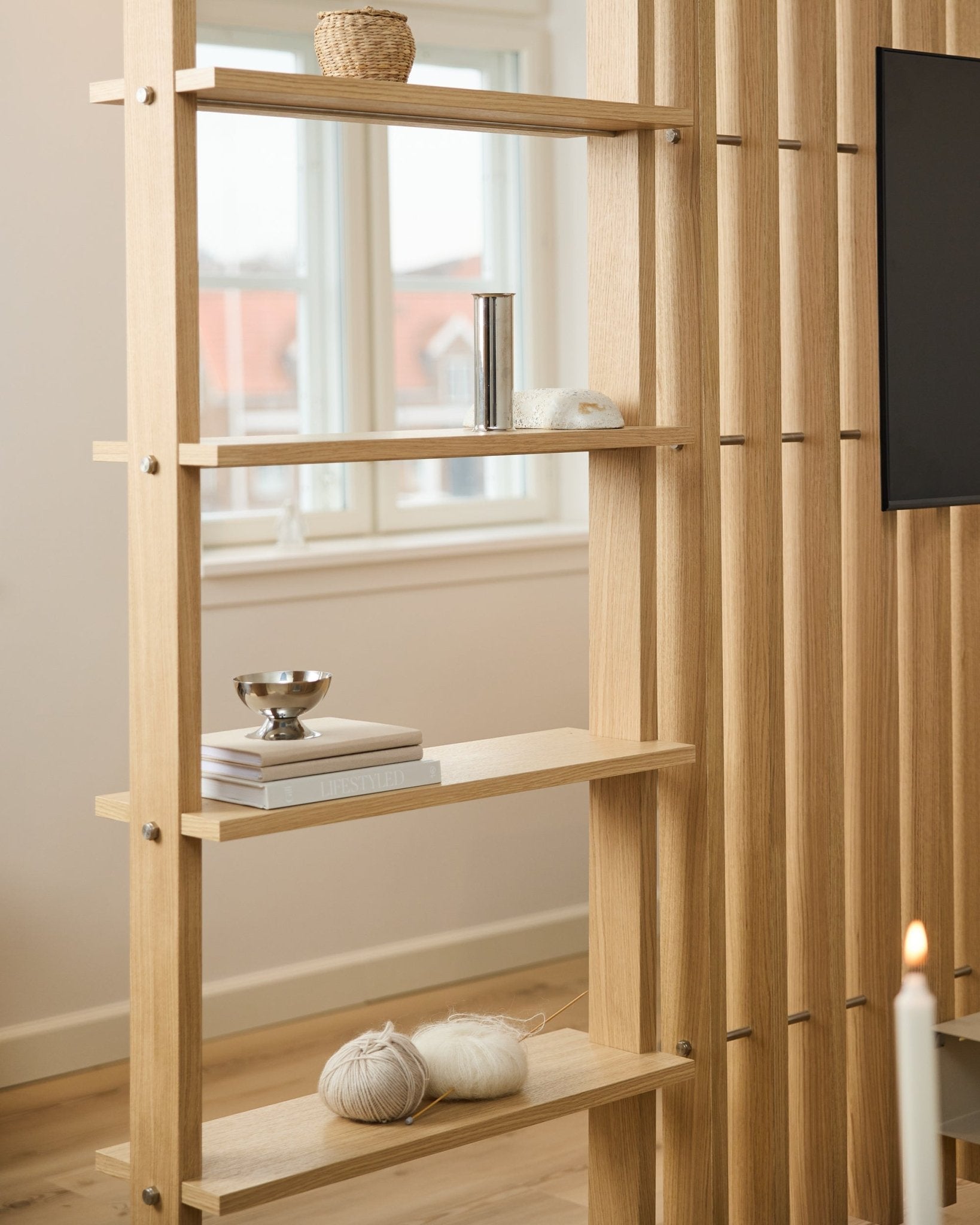 Heller Eichenholz-Raumteiler von WoodUpp mit vertical Lamellen und Regalböden mit Büchern und Strickgarn.