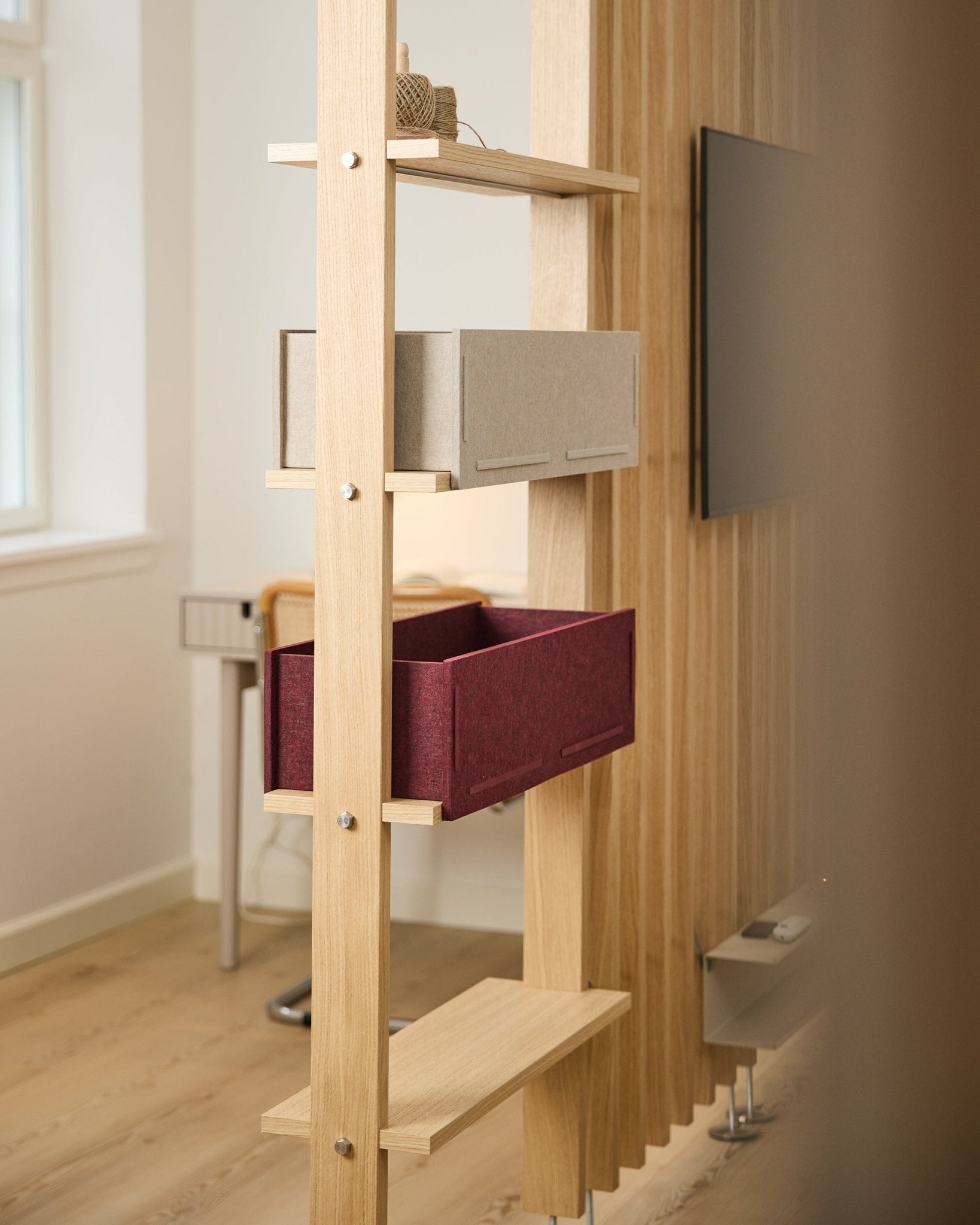 Ein Regal von WoodUpp zeigt eine Aufbewahrungsbox in beige und eine ox red Vigg Felt Box / BM2 in einem hellen, minimalistischen nordischen Raum mit akustischen Holzdetails.