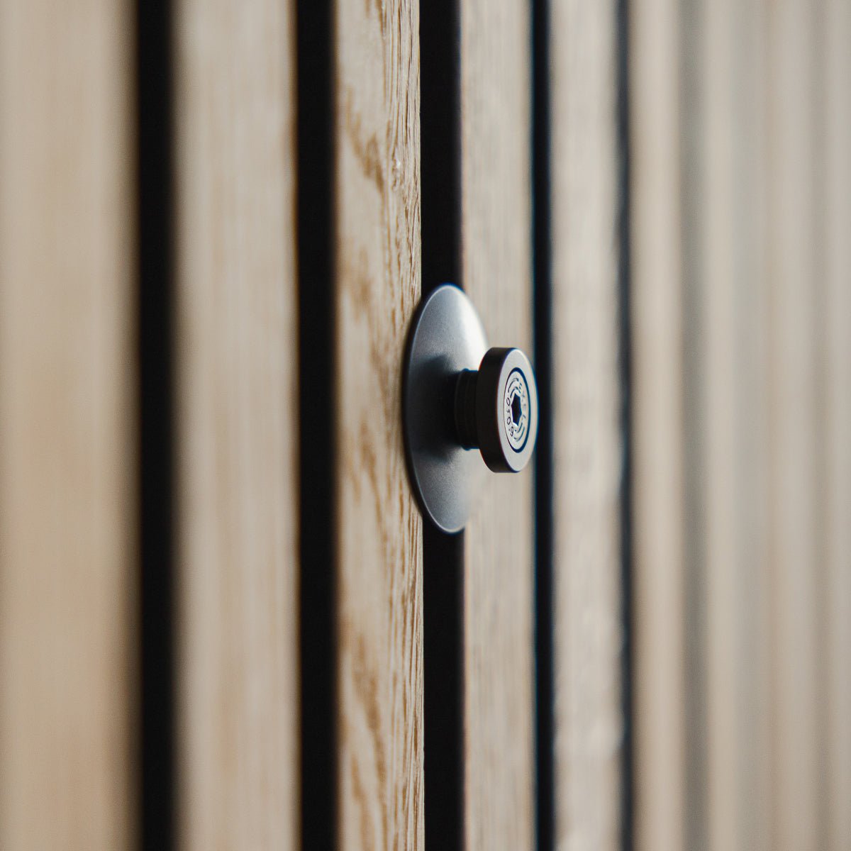 Nahaufnahme des Dupps | Heavy Türspions von WoodUpp aus black Aluminium, montiert in einer gerillten Holztür mit Akupanel Akustiklamellen, die Linse im Fokus.